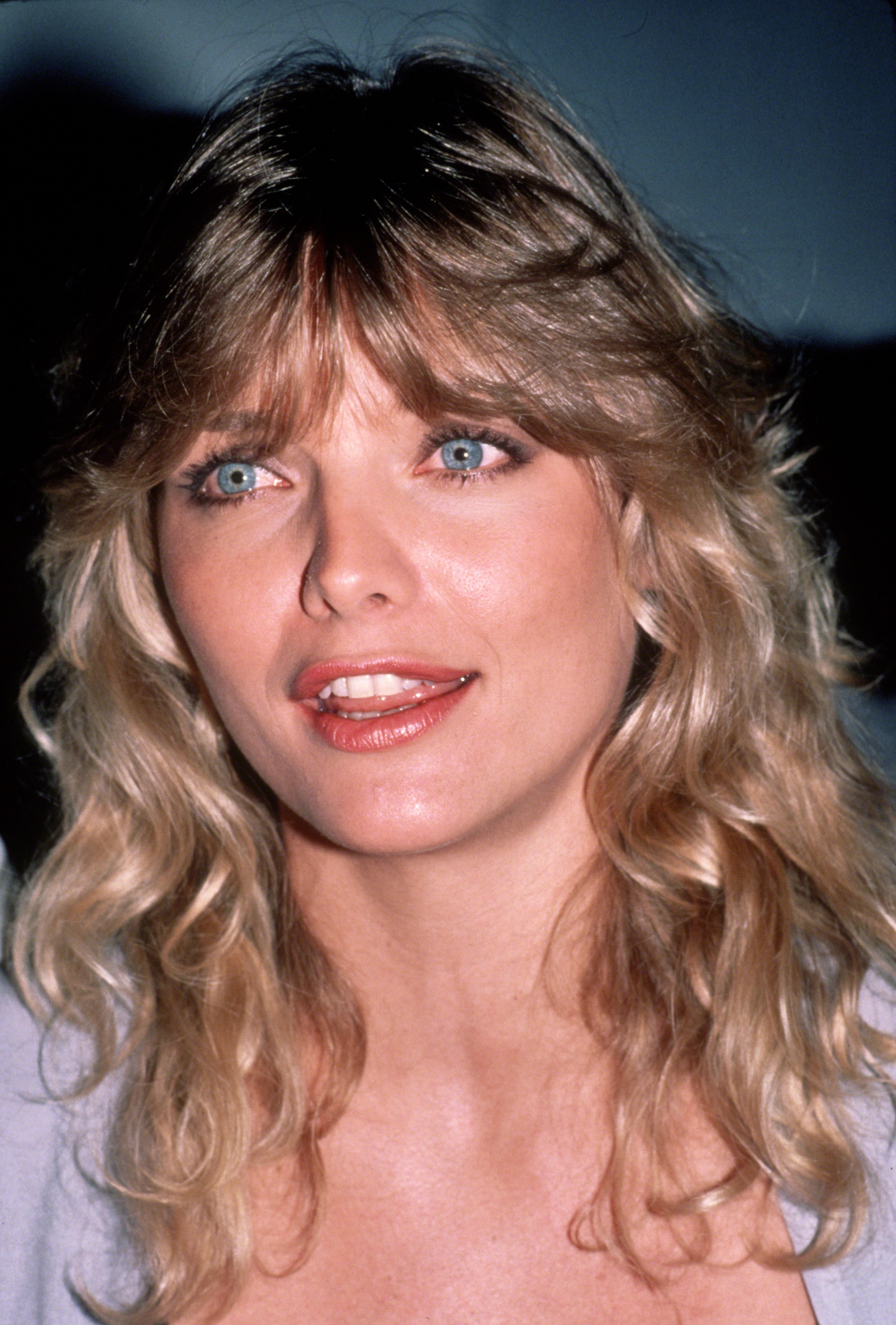 Person with wavy hair and a light top, smiling