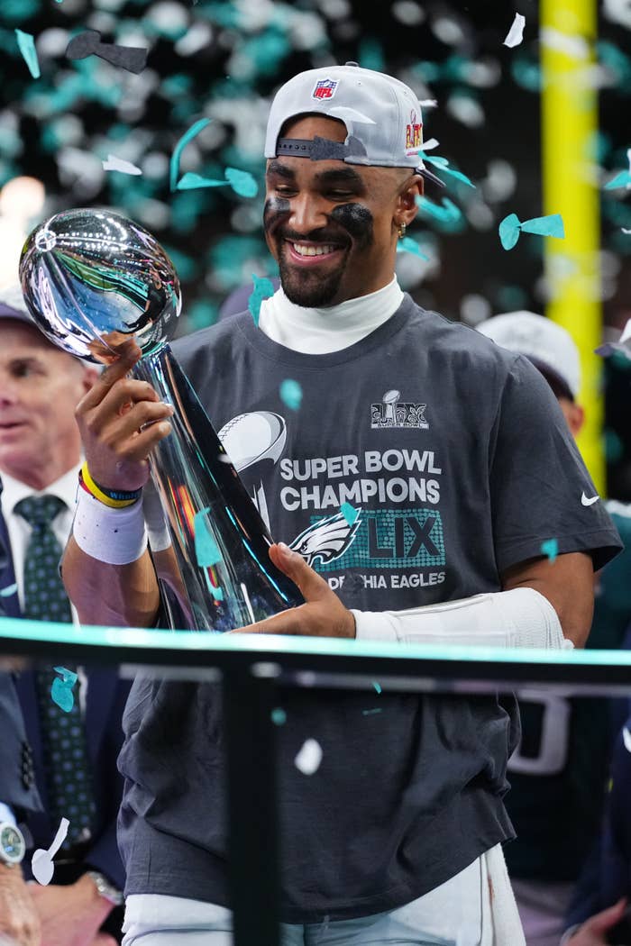 Jalen Hurts holding a Super Bowl trophy, wearing a t-shirt with