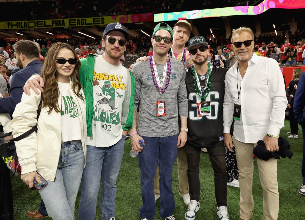 A group of casually dressed people poses on a sports field, some wearing Philadelphia Eagles-themed clothing