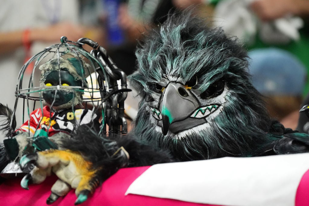 A person in a detailed bird costume holds a miniature bird replica in a wire cage