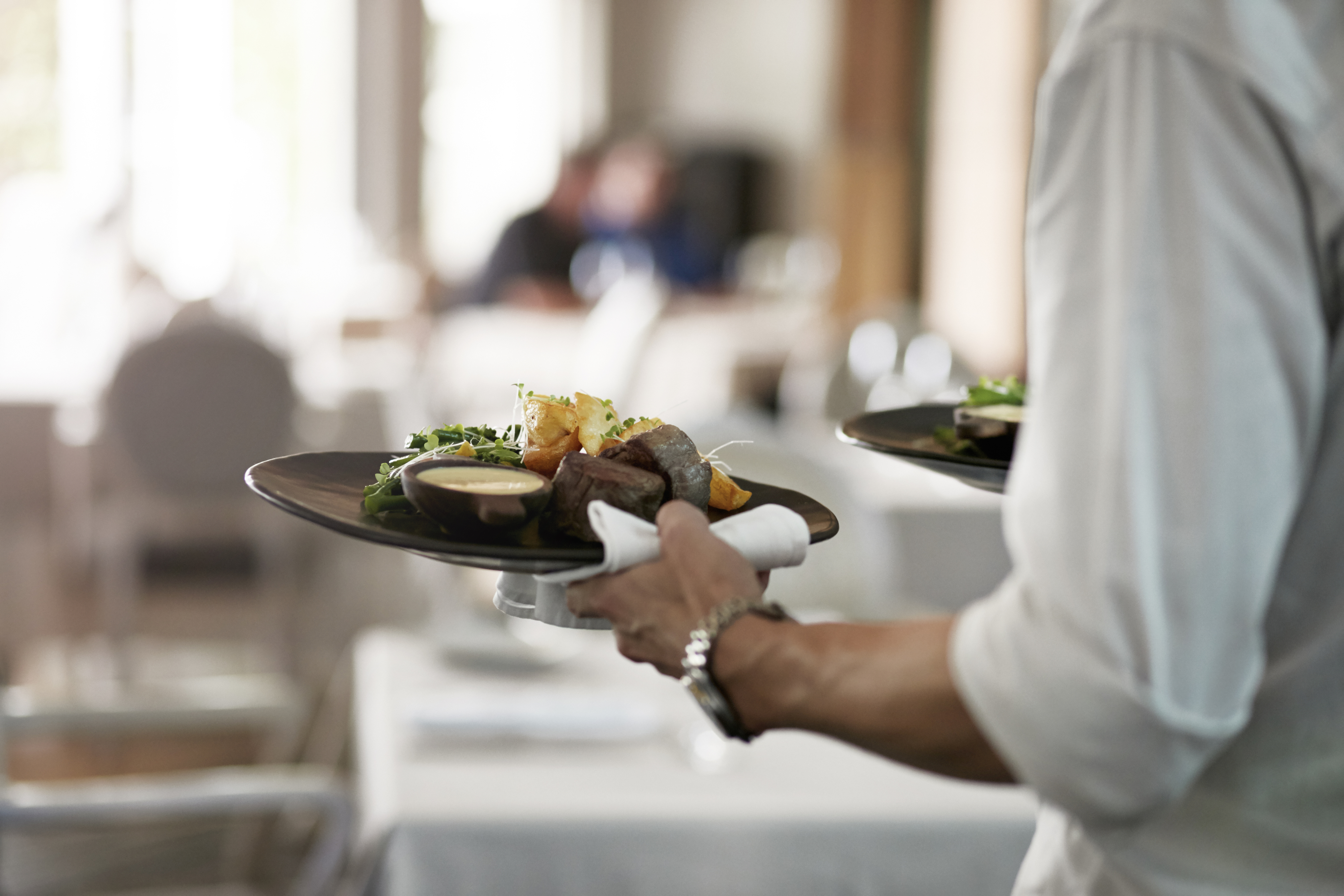 Server som har en gourmetrett med biff, poteter og grønnsaker i en stilig restaurantinnstilling