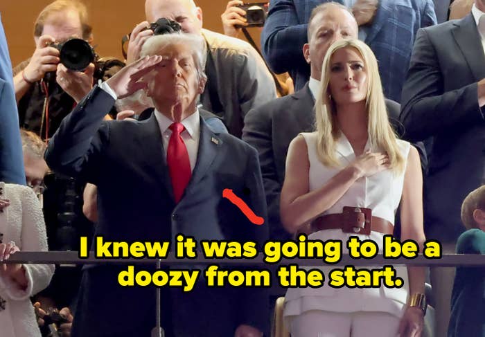 A man in a suit salutes while a woman in a white outfit stands with hand on chest, surrounded by photographers