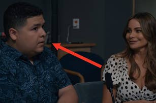 Two people sitting together, one in a floral shirt, and the other in a polka dot dress, smiling and talking in an indoor setting