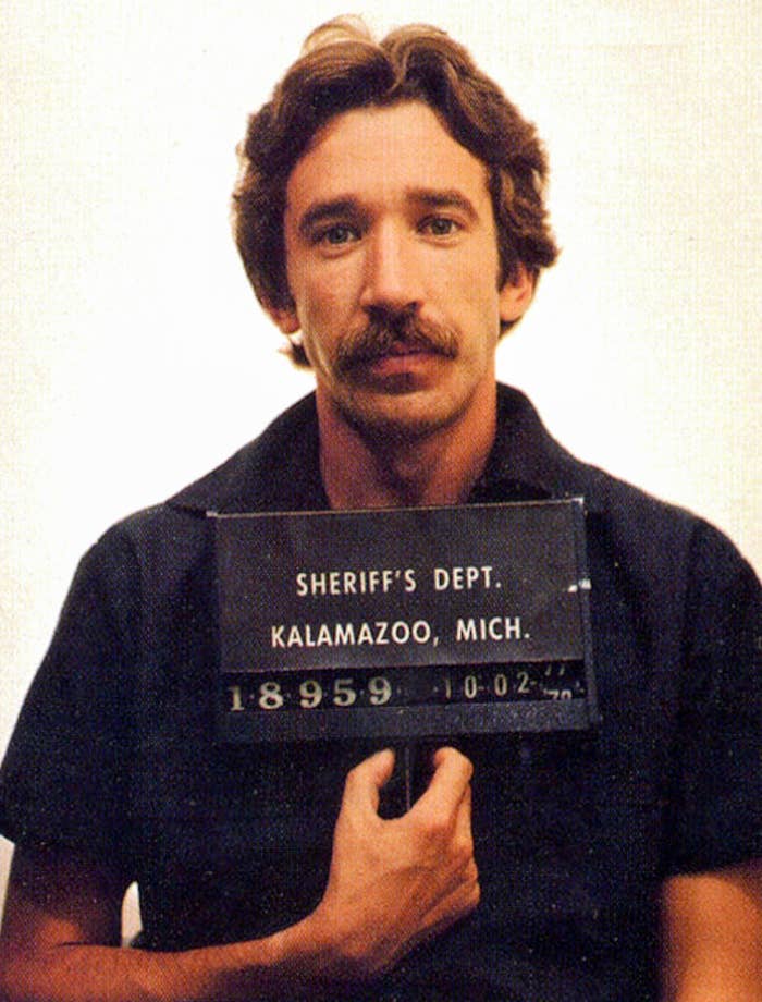 A man with a mustache holds a placard reading