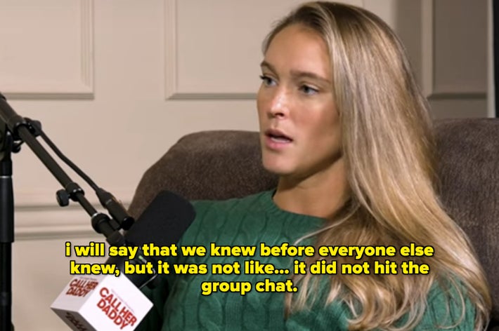 Kylie Kelce seated in an armchair speaking into a microphone, wearing a green cable-knit sweater and jeans, with a plant in the background