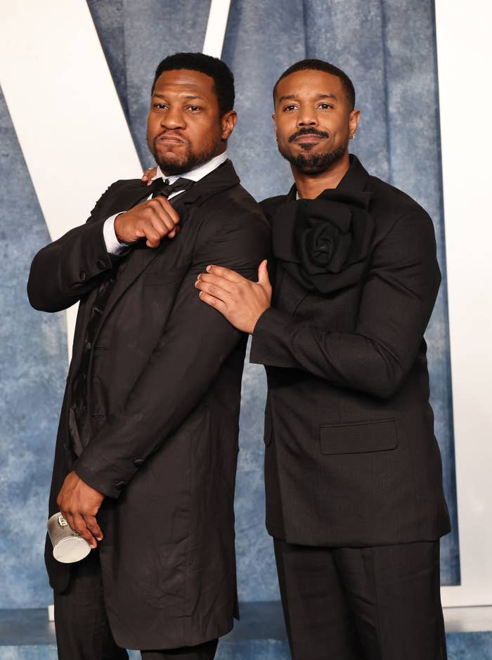 Jonathan Majors and Michael B. Jordan in stylish black suits pose confidently together at a formal event, showing camaraderie and elegance