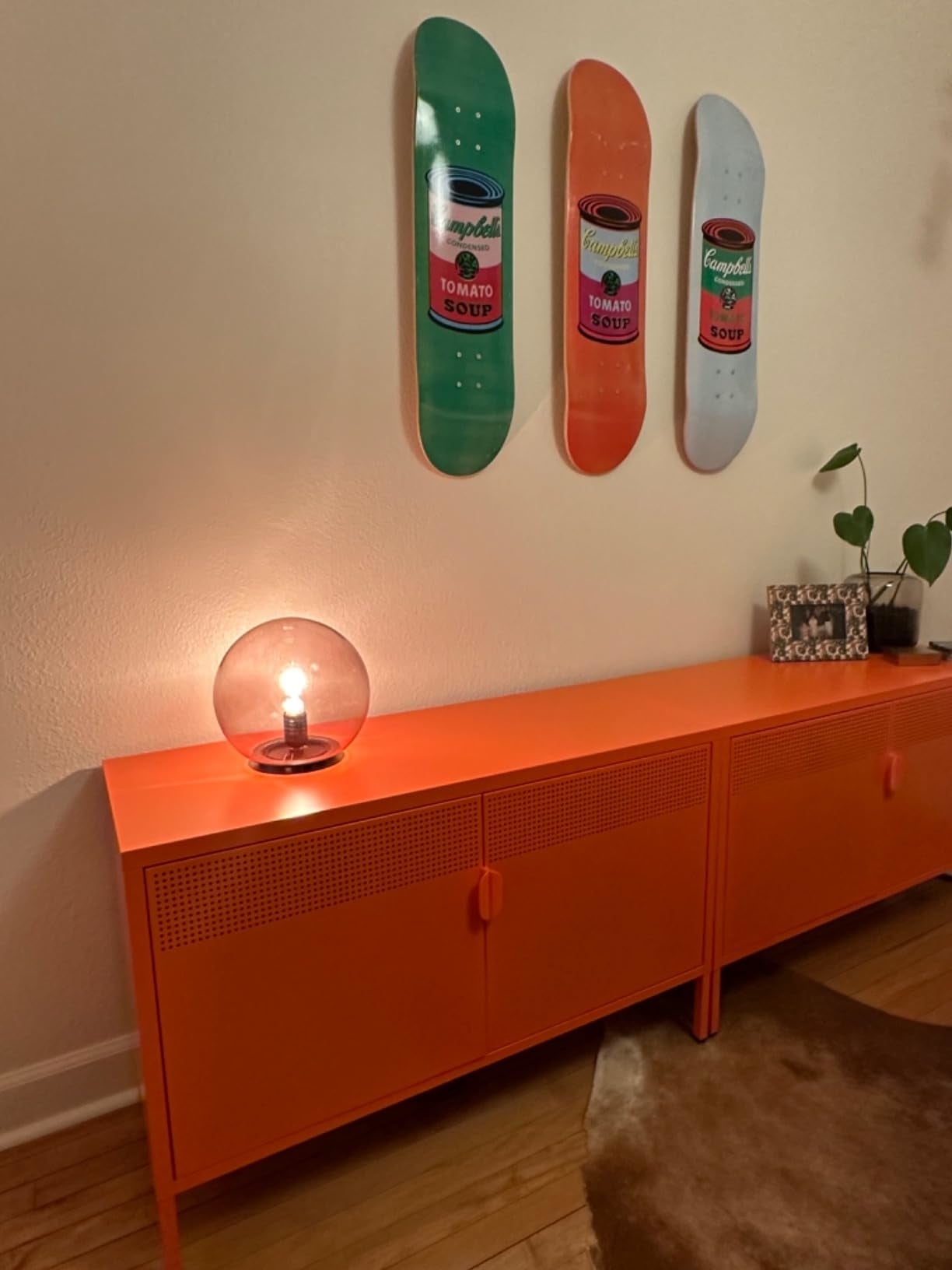 Room with orangish  sideboard, circular  lamp, and wall-mounted skateboards featuring crockery   tin  designs. Stylish location  decor