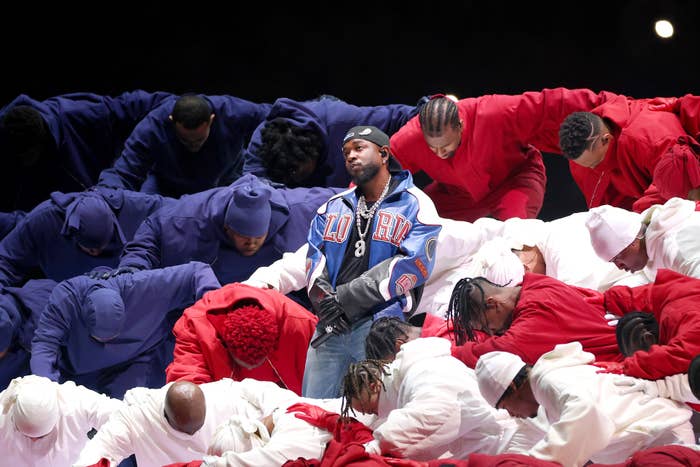Kendrick on stage in center wearing a varsity jacket, surrounded by dancers in coordinated red, white, and blue outfits