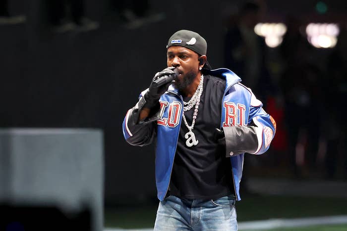 Kendrick performing on stage, wearing a varsity jacket, a backwards cap, and gloves, with a prominent necklace