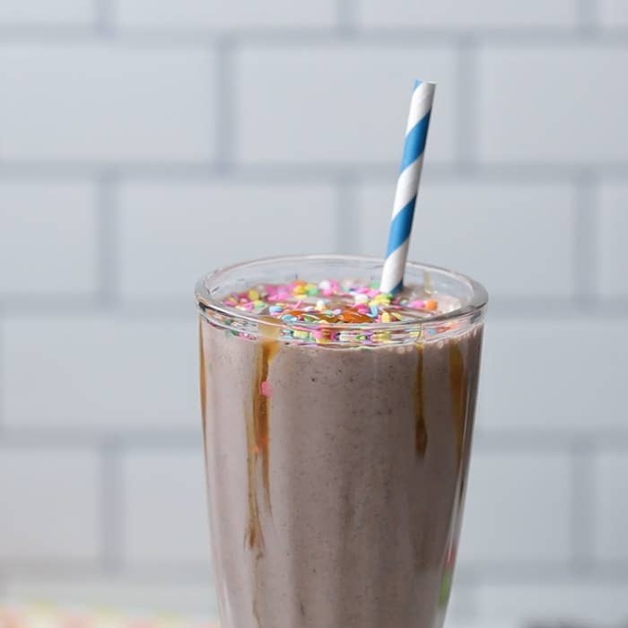 Milkshake in a glass with sprinkles on top and a striped straw, set against a tiled background