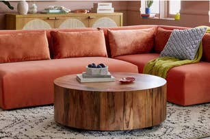 Modern orange sectional sofa with textured pillows is paired with a round wooden coffee table on a patterned rug. Cozy living room setup