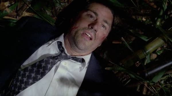 Person in a suit, lying on the jungle floor, looking up with a concerned expression