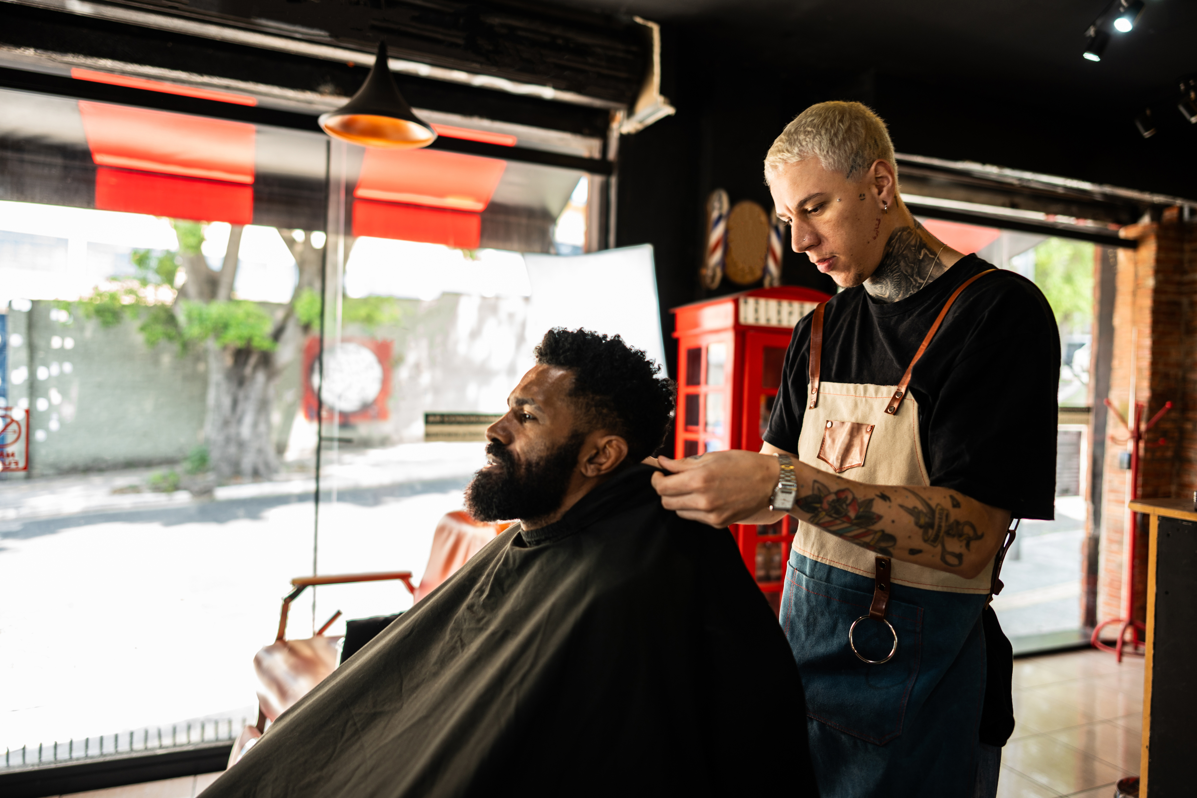 Frisør med tatoveringer kutter en manns hår i en moderne frisørbutikk i en moderne barberbutikk