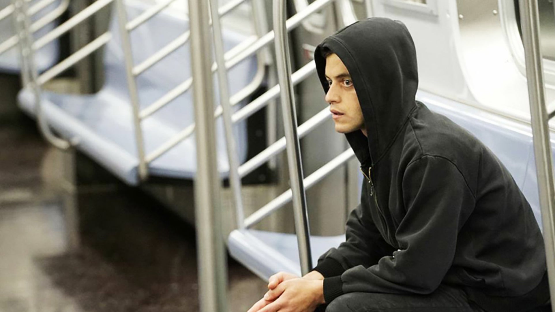 Person wearing a hoodie sitting in a subway car, appearing deep in thought