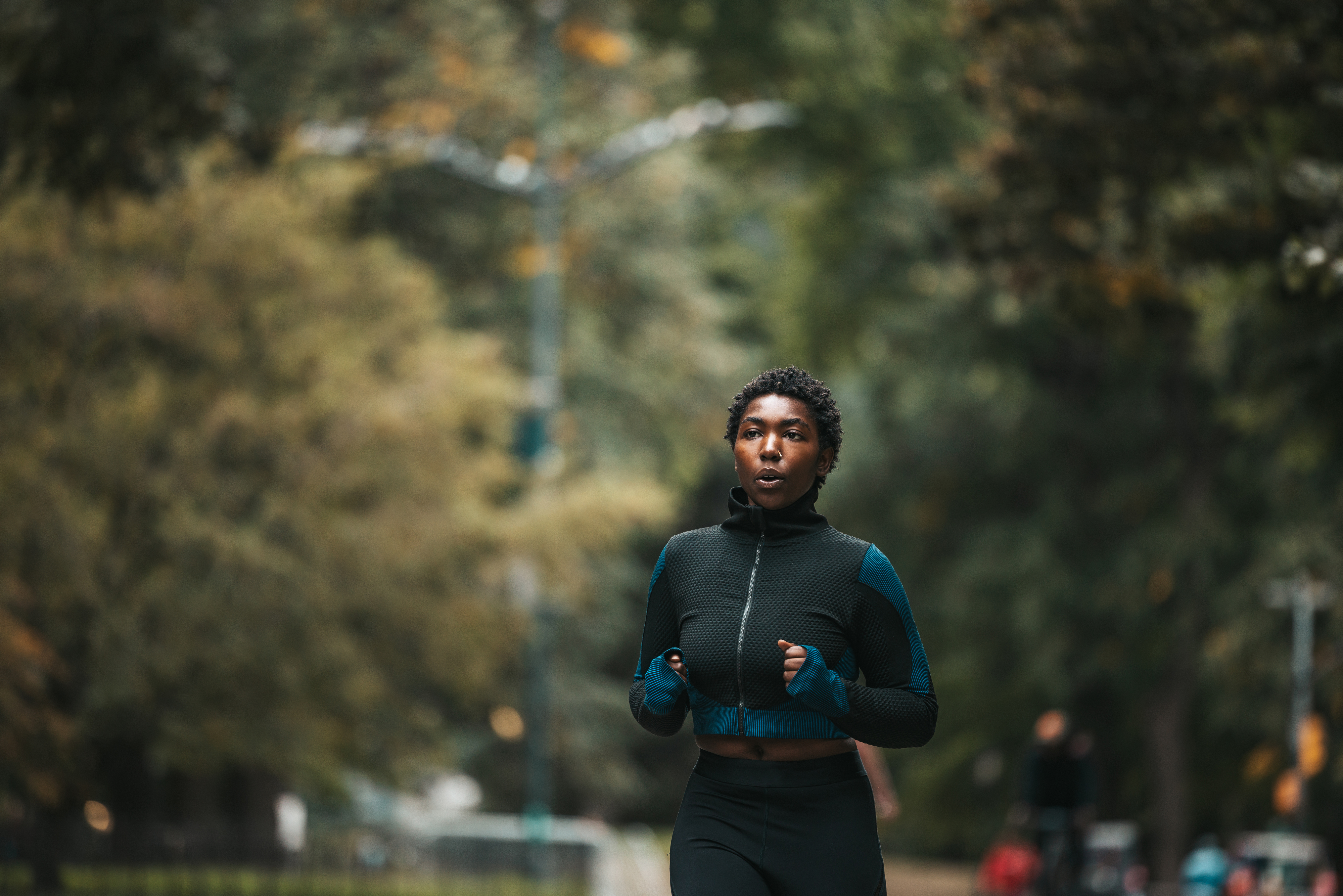 Person Jogging i en park, iført en zip-up atletisk jakke og leggings, med trær i bakgrunnen