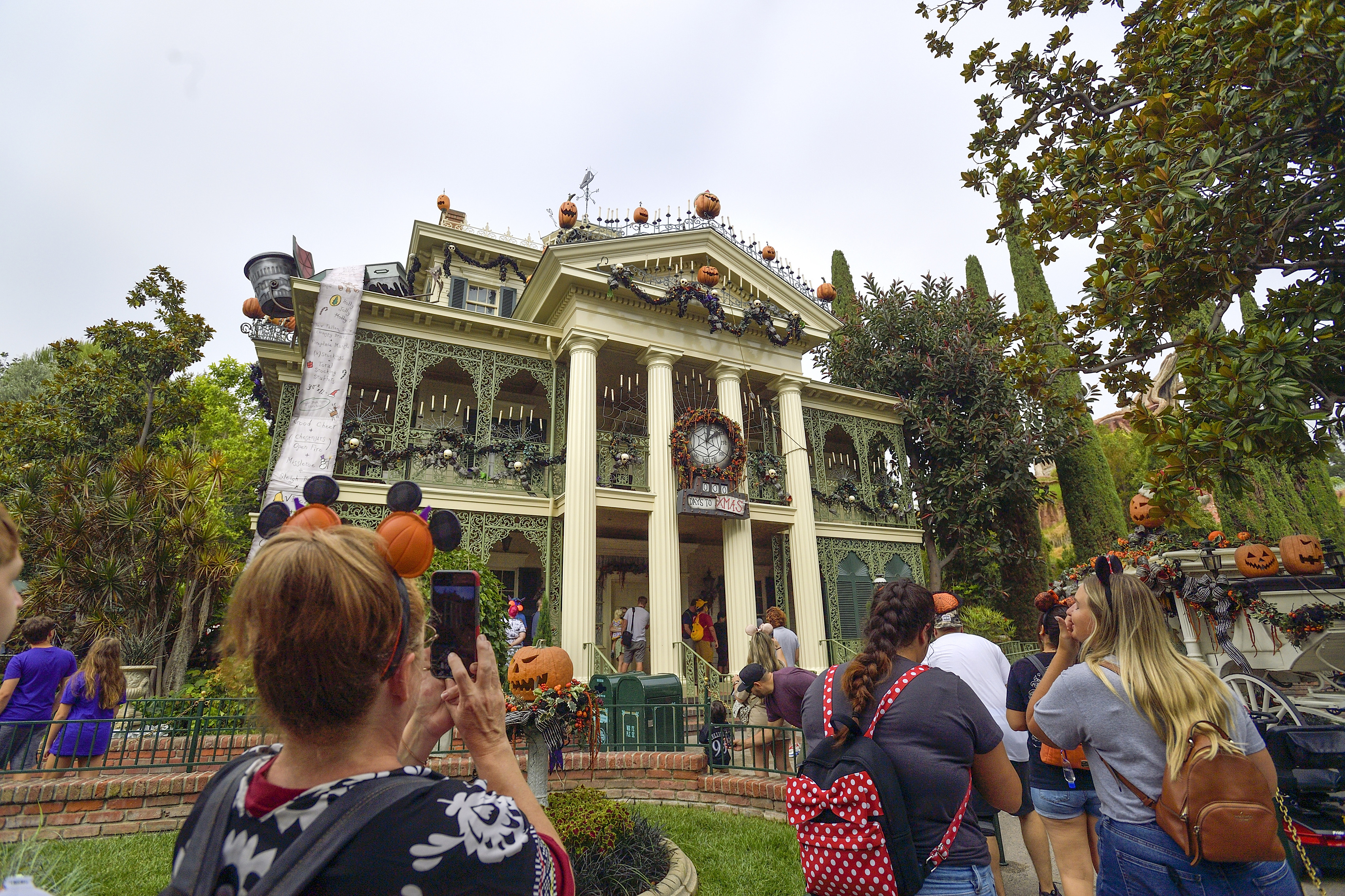 People visiting a decorated mansion with Halloween-themed ornaments and pumpkins, taking photos and enjoying the festive atmosphere