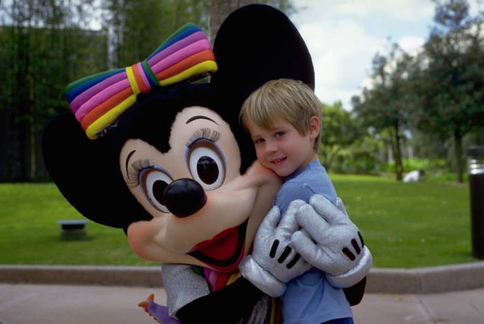 Child hugs Minnie Mouse mascot outdoors in a park setting