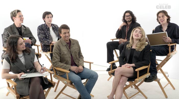 Group of seven people, including Ralph Macchio, seated on director chairs, smiling and interacting in a relaxed, casual setting