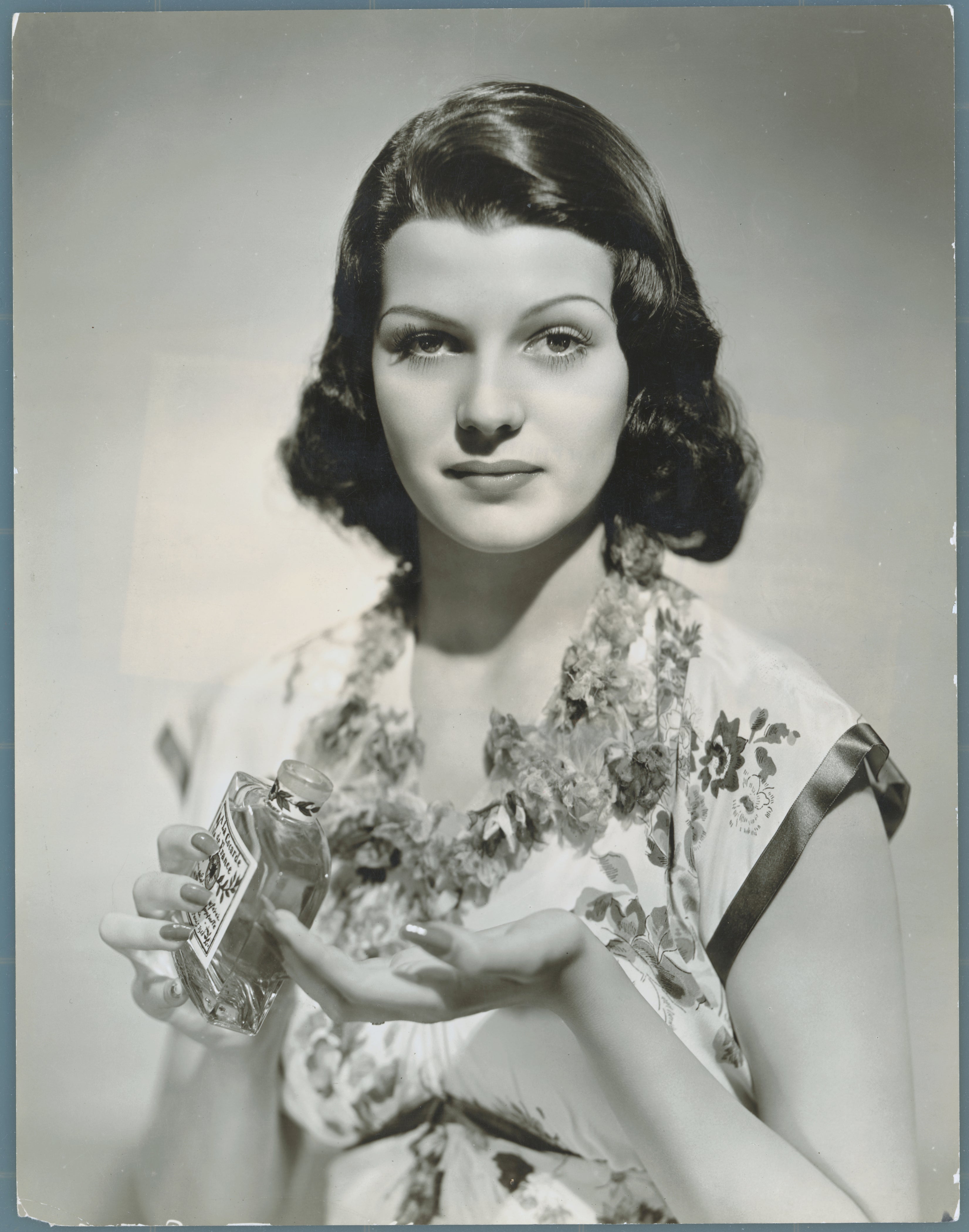 Person holding a bottle, wearing a floral dress, styled with vintage Hollywood elegance. Classic, timeless beauty is captured in the image