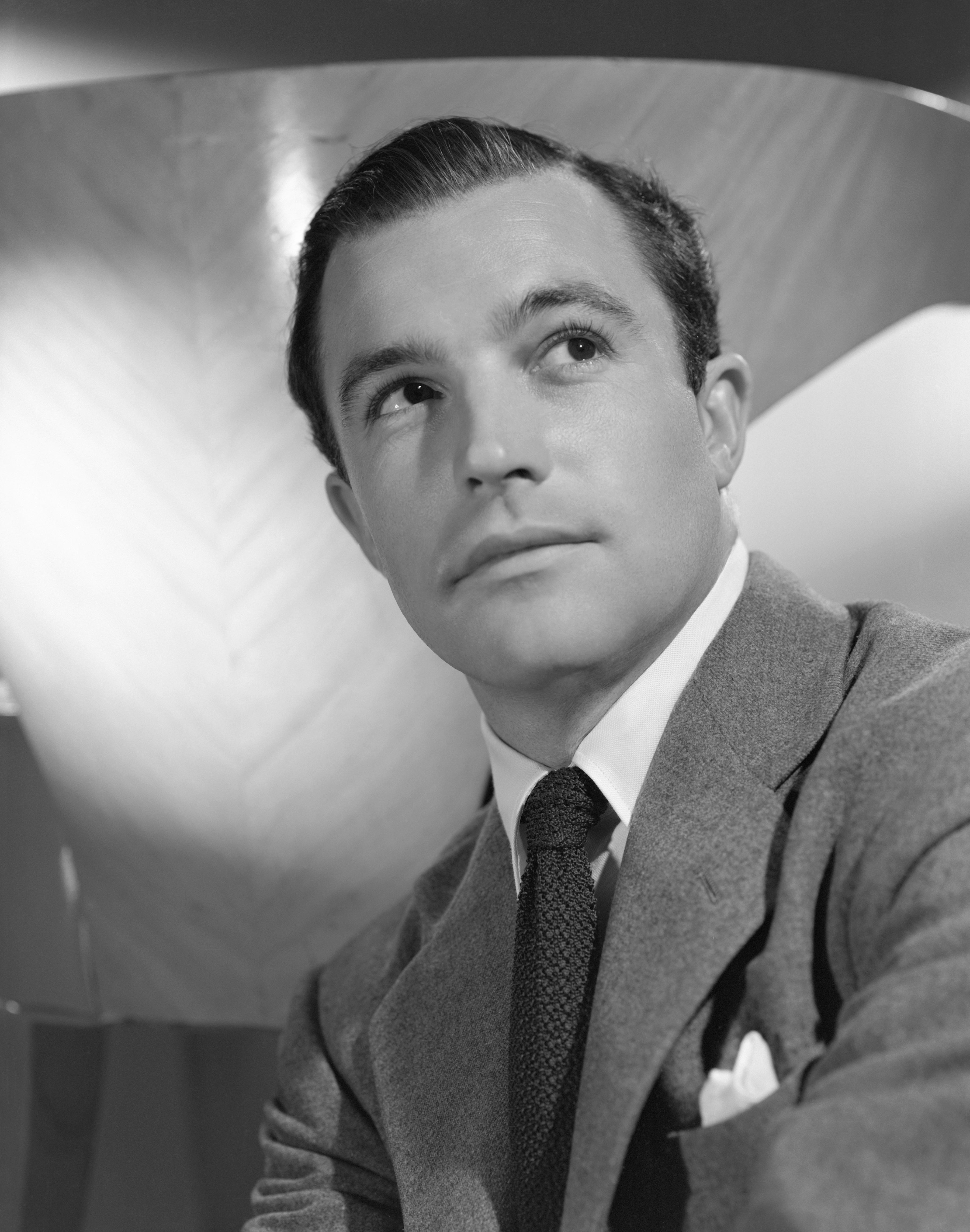 A person in a classic suit and tie looks upward thoughtfully in a professional black and white portrait