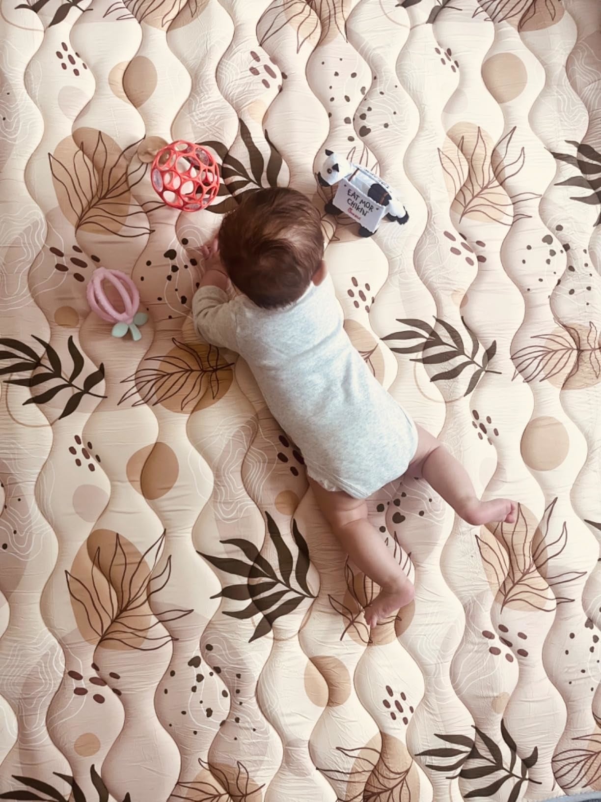 Baby lying connected  a patterned playmat with toys scattered around