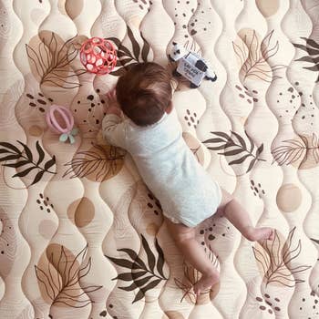 Baby lying connected a patterned playmat with toys scattered around