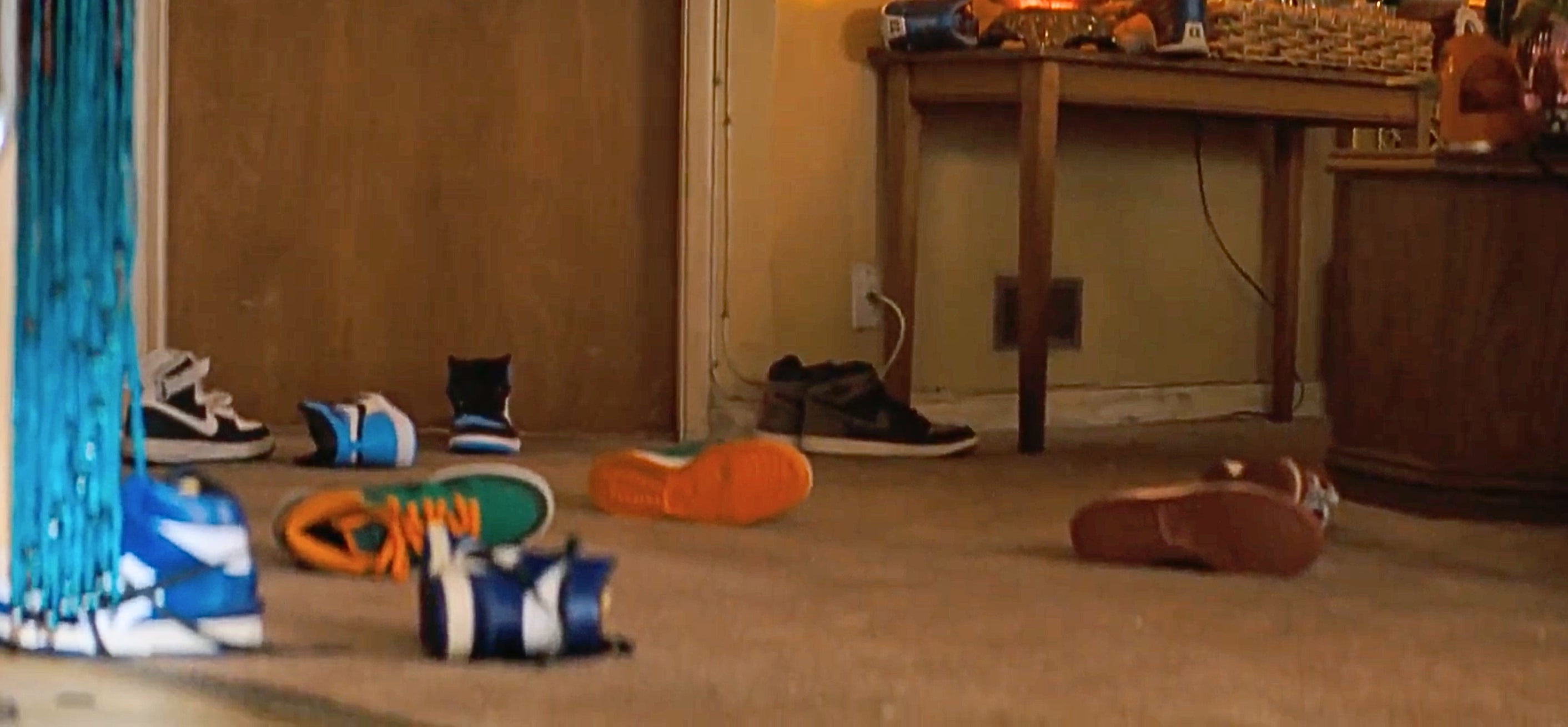 Several sneakers scattered on a carpeted floor in a room with a wooden table in the background