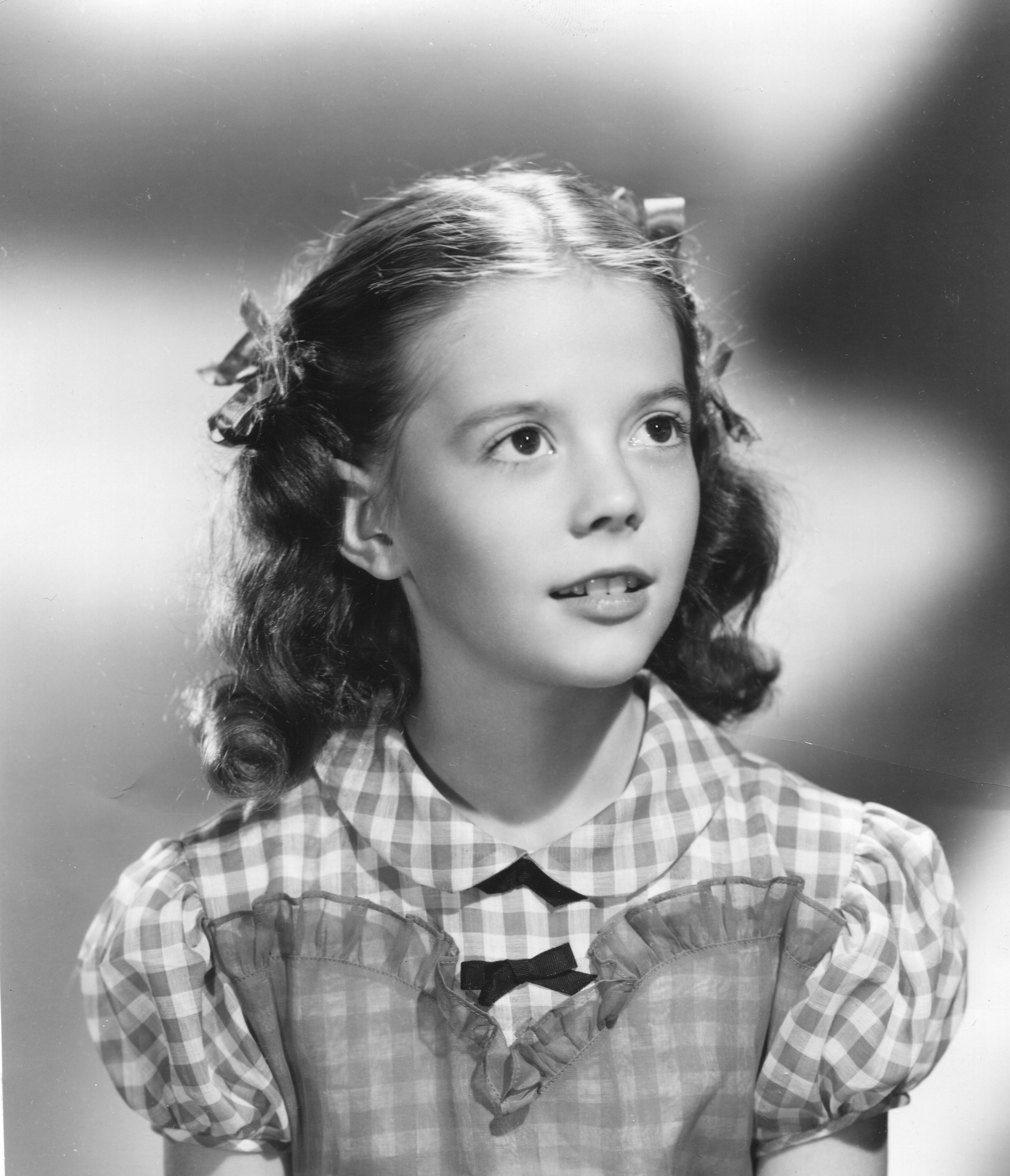 Young girl in vintage gingham dress with ribbons in curly hair, looking upward thoughtfully