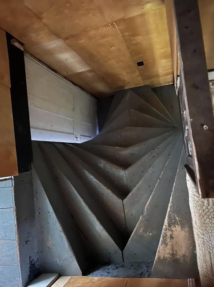 Modern, sculptural staircase with sharp, angular steps and a minimalist design, seen from above in a dimly lit setting