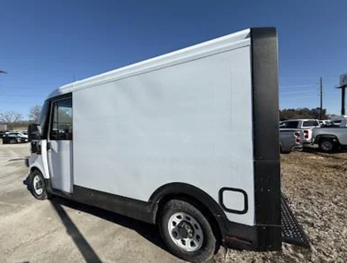 Delivery truck parked outdoors, viewed from the side, with a large storage area and black side accents