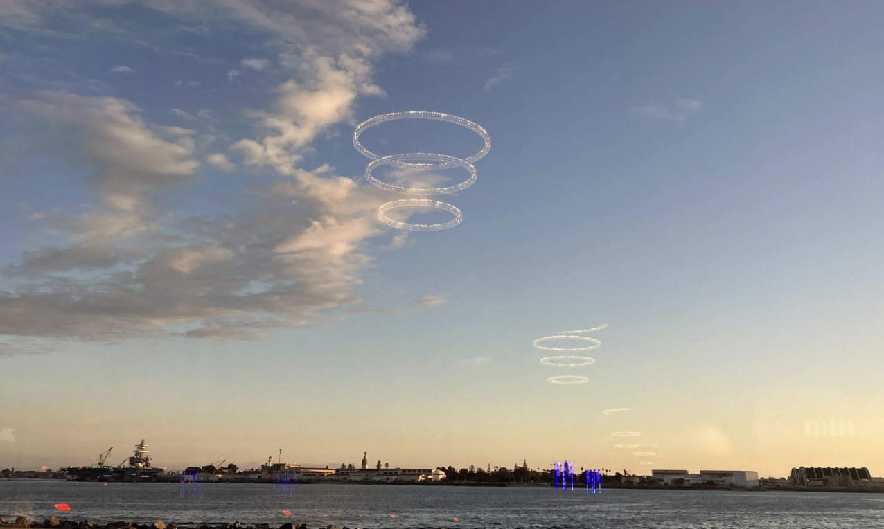 Circular light patterns hover over a body of water, with ships and buildings on the horizon under a partly cloudy sky