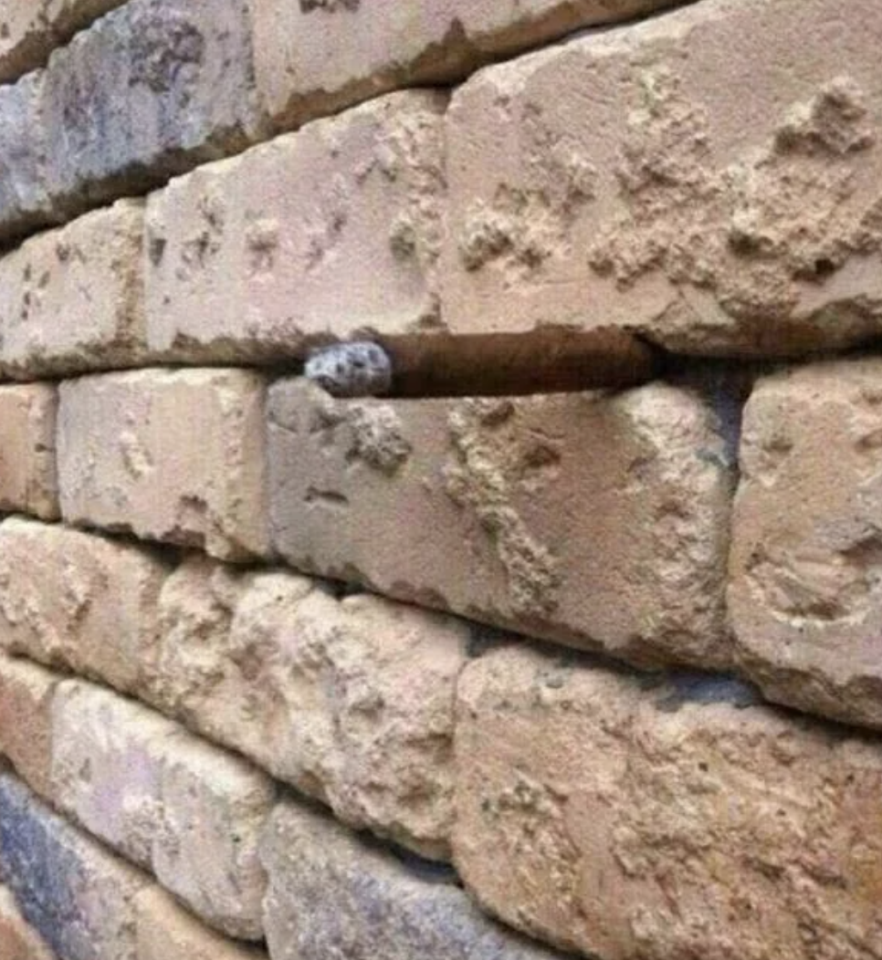 Stone wall with an optical illusion of a misplaced brick appearing to stick out, resembling a cigar