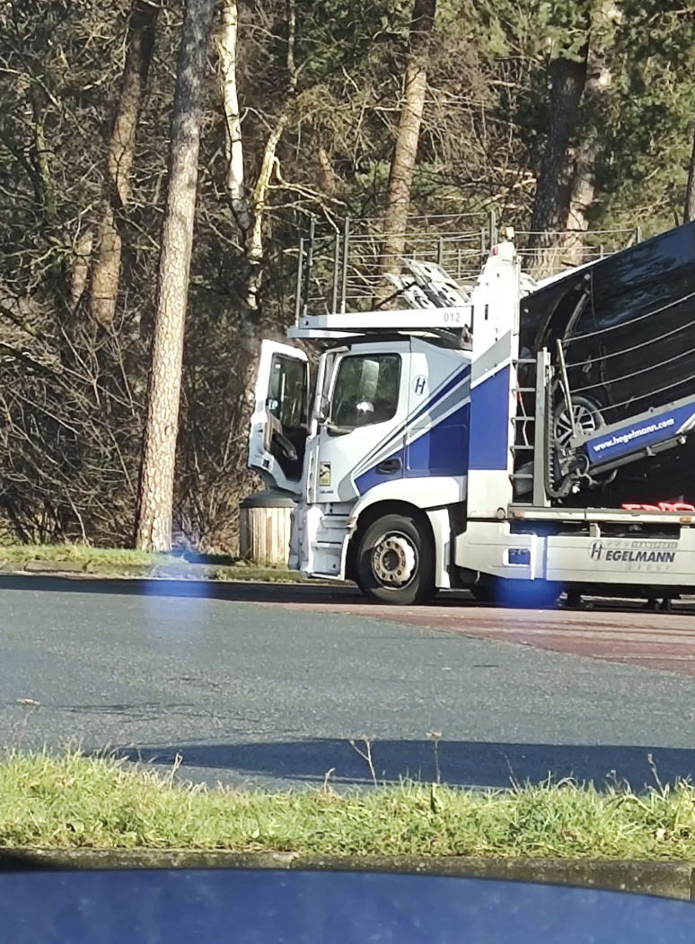 Flatbed truck parked beside a forest with a blue hydraulic system visible