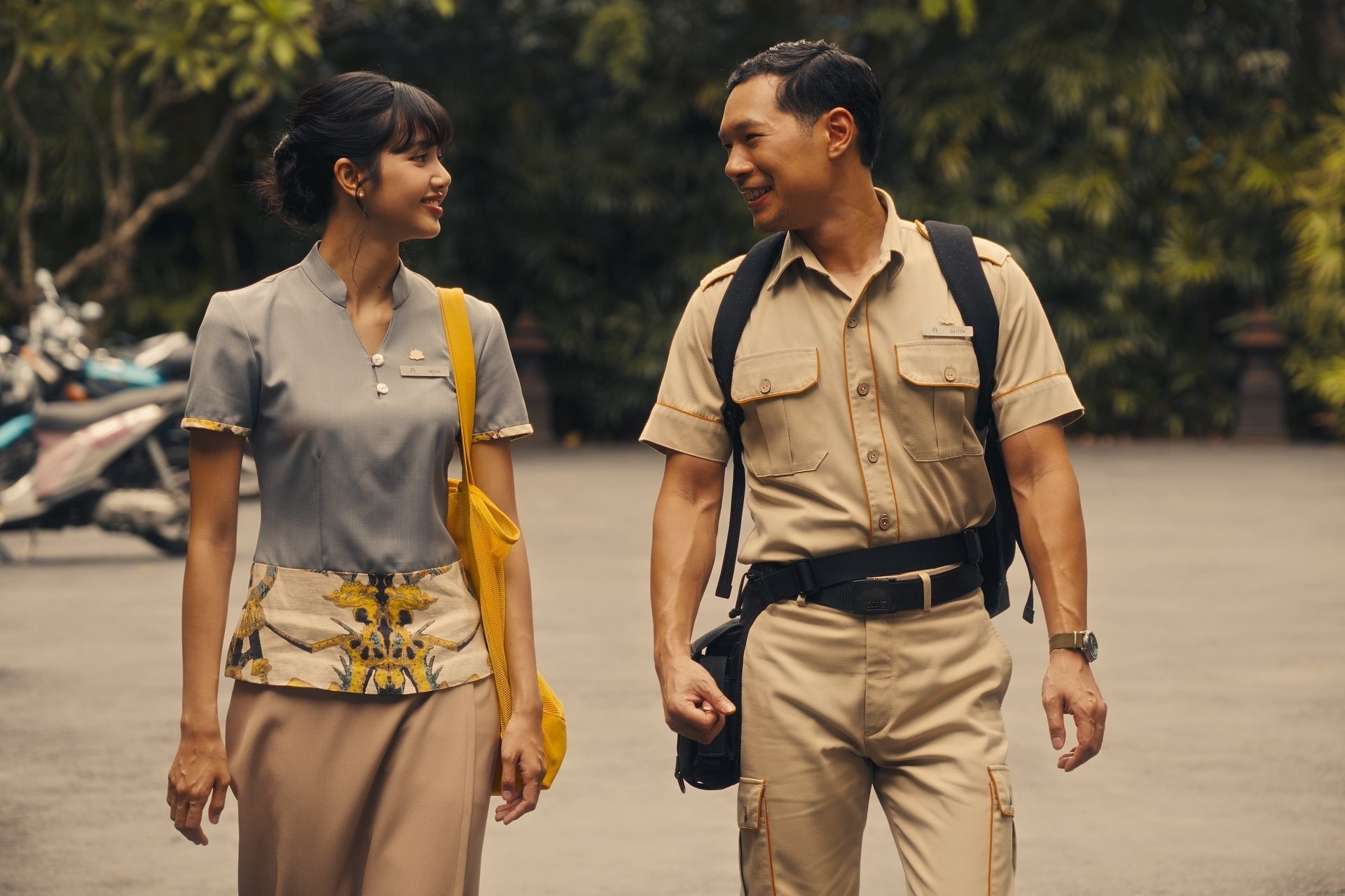 Two people in uniform are walking and smiling at each other, suggesting they're part of a scene from a TV or movie production