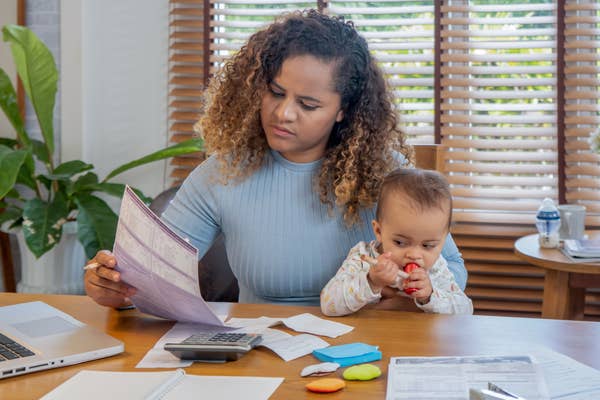 Person at a table handling papers and a calculator, while holding a baby chewing on a toy