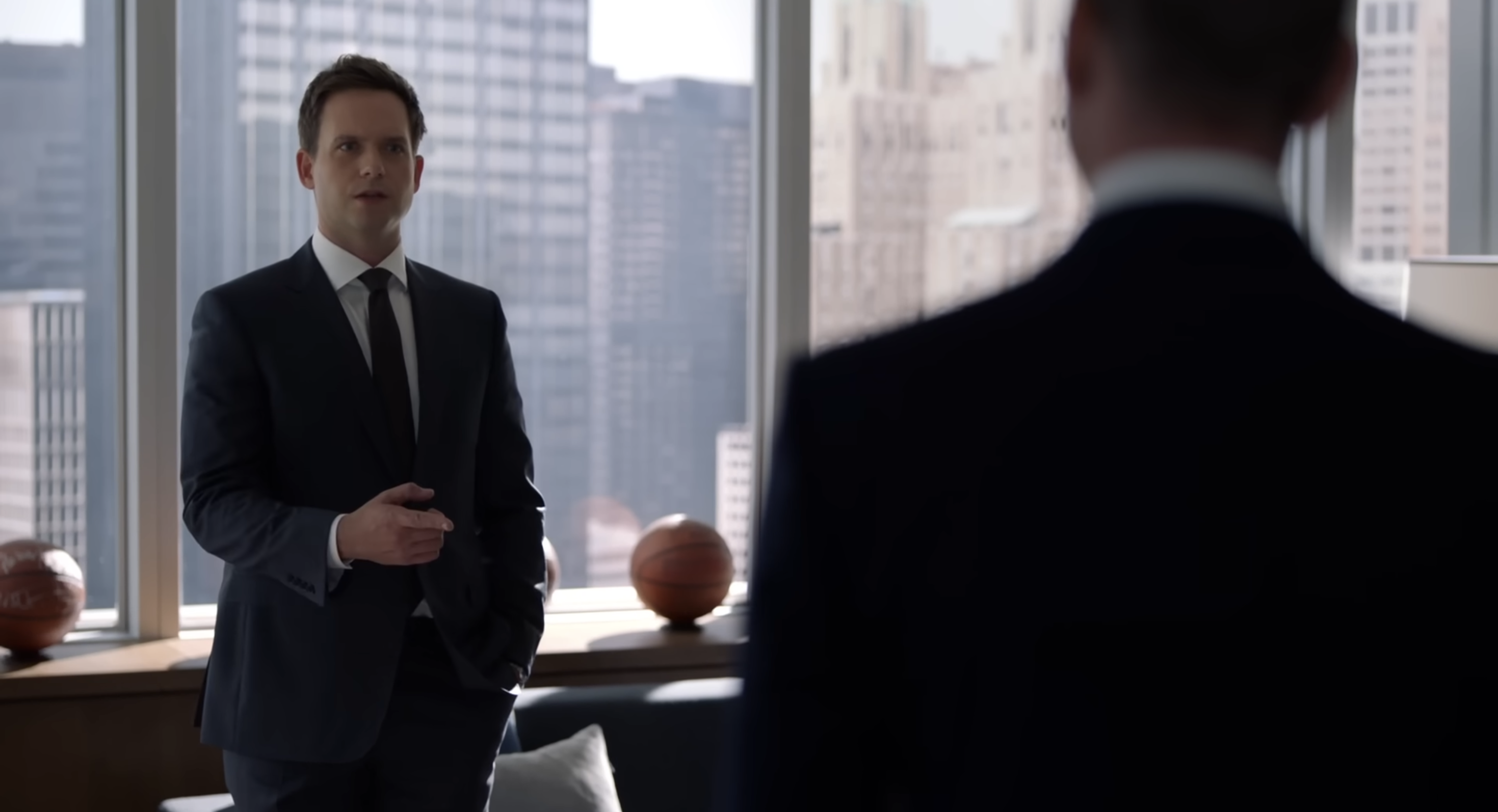 Two men in suits are having a conversation in a modern office with a city view