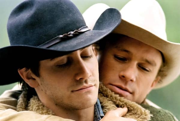 Two actors embrace tenderly wearing cowboy hats and jackets, portraying a scene from a well-known film