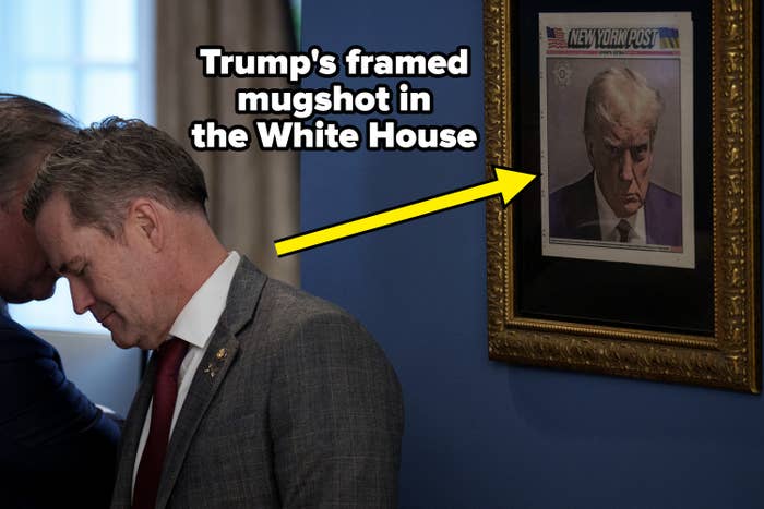 A person in a suit looks down beside a framed New York Post cover featuring a serious portrait of Donald Trump