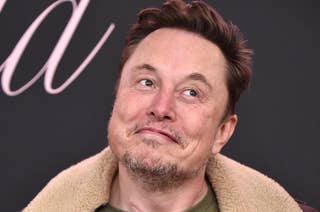 Elon Musk in a shearling-lined jacket and casual shirt making a quirky facial expression at an event