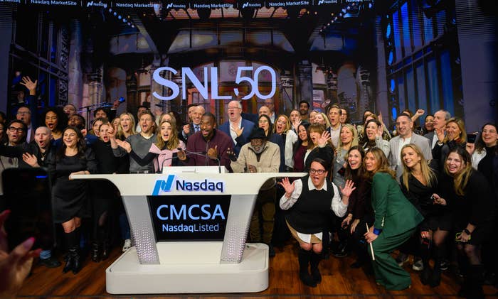 Group photo of people at a Nasdaq event for SNL's 50th anniversary, with a mix of formal and casual outfits