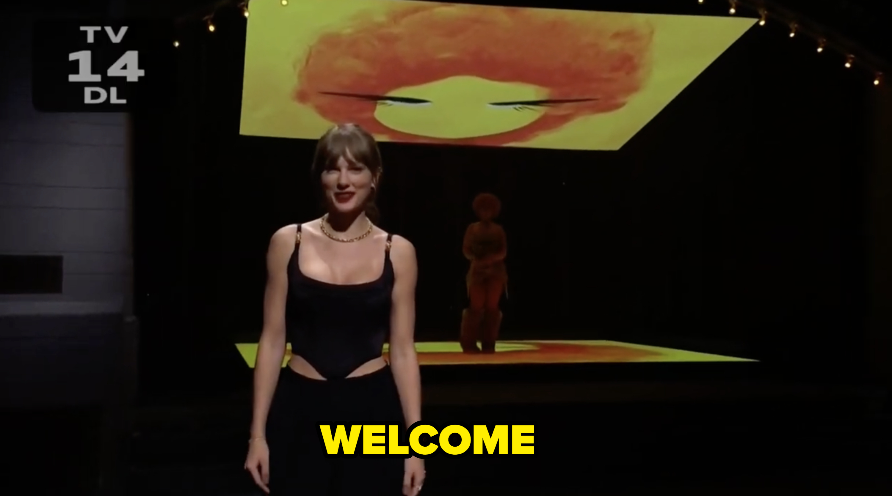 Taylor Swift on stage in sleek outfit, with abstract art projected above and behind her on a large screen