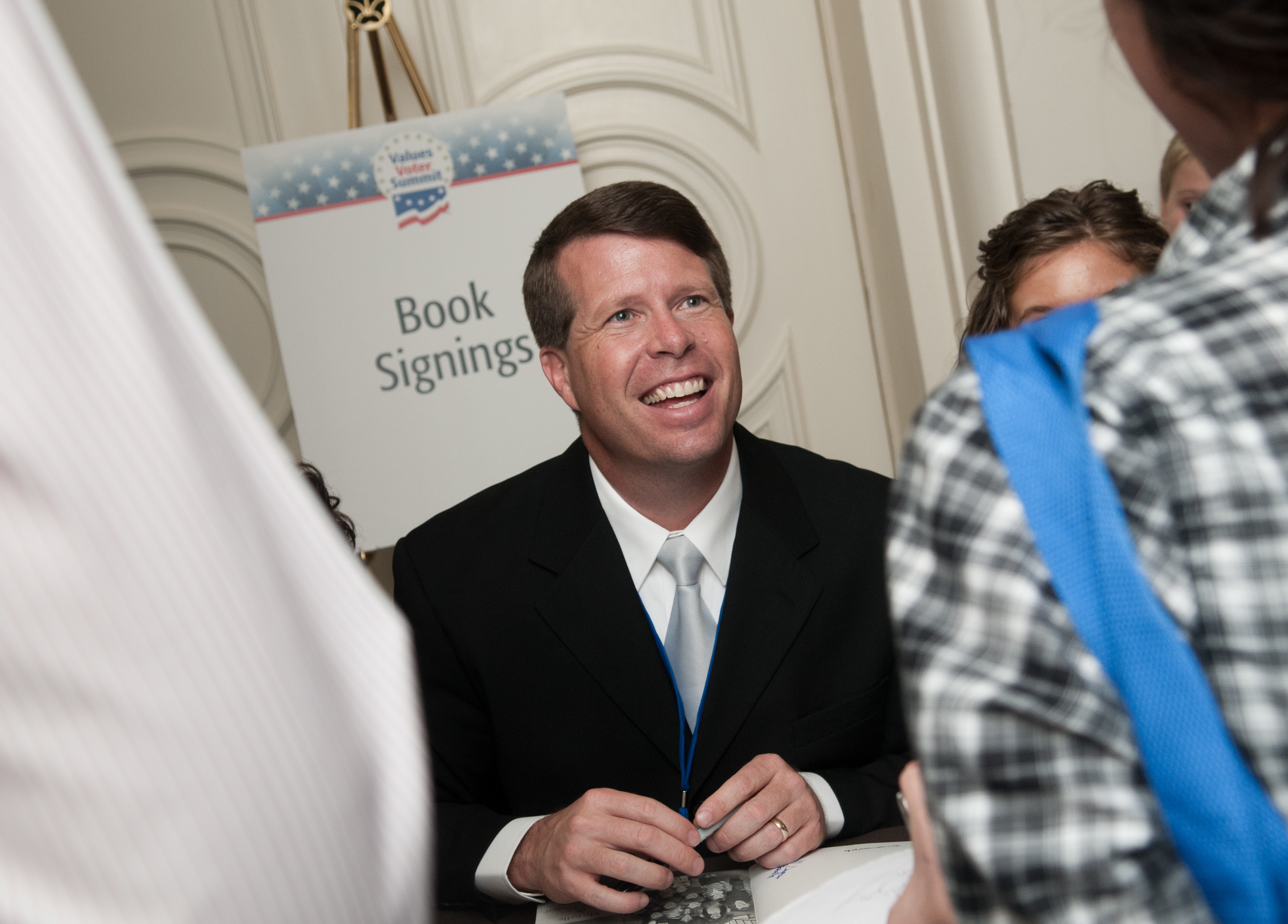 Jim Bob Duggar in a suit at a book signing event, smiling and interacting with attendees.