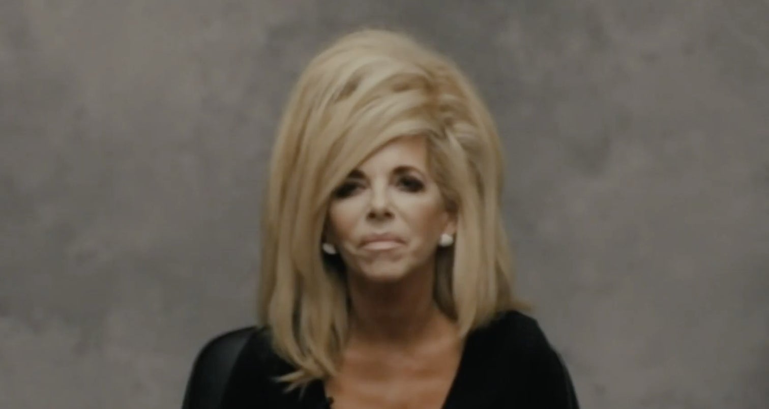 Gwen Shamblin sits against a grey backdrop, she has large, voluminous hairstyle, and is wearing a dark top.