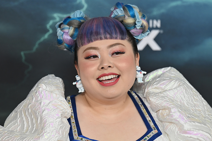 女性が特徴的な編み込みヘアと大きな白いドレスを着用し、笑顔で写っている。背景にはイベントの文字が見える。