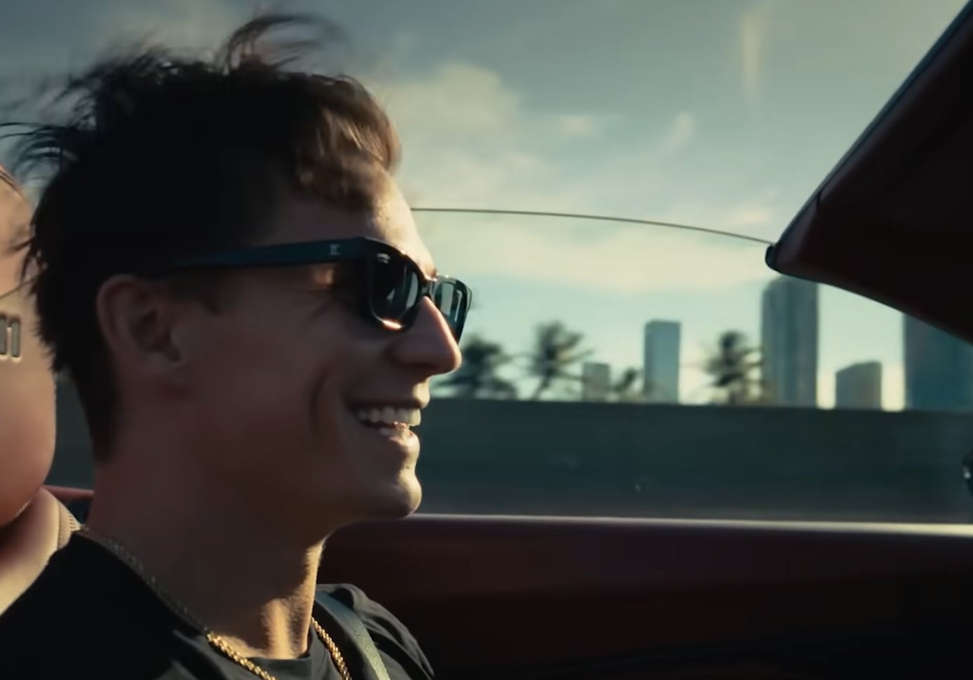Person smiling while driving a convertible with cityscape in the background