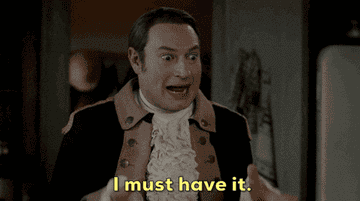 A person in historical attire excitedly gestures, saying, &quot;I must have it,&quot; with a playful expression