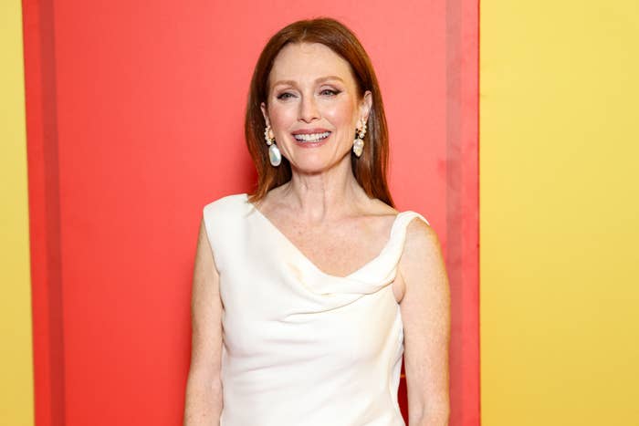 Person in elegant white gown and statement earrings, smiling on a red carpet background