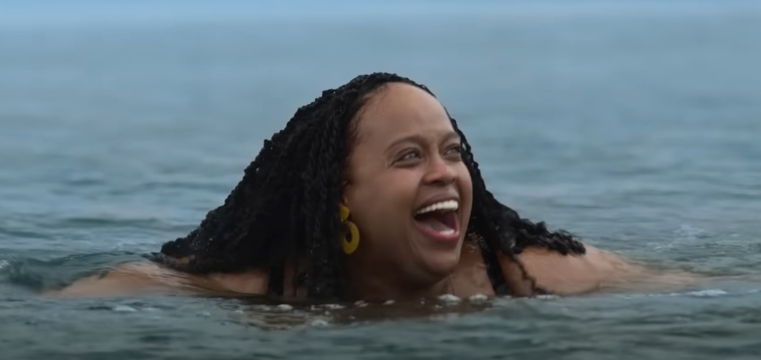 Person joyfully swimming in the ocean, wearing large hoop earrings