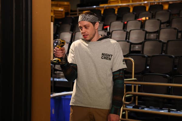Person in a &quot;Night Crew&quot; T-shirt, bandana, and holding a drill in an empty auditorium