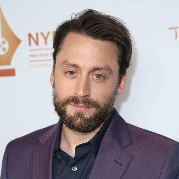 Man in a purple suit jacket and dark shirt at a formal event
